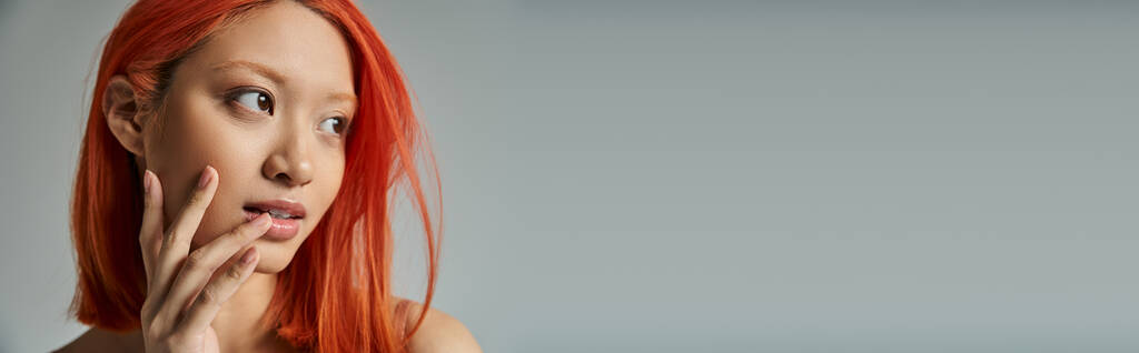 belleza asiática, mujer joven con el pelo rojo y maquillaje natural mirando hacia otro lado y tocando mejilla, bandera - Foto, Imagen