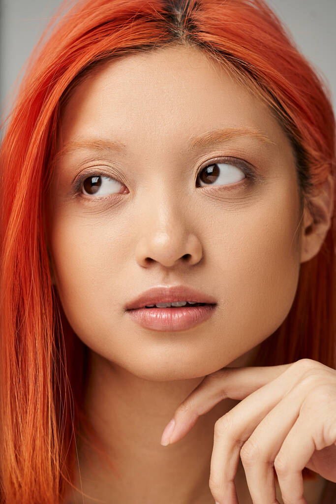Nahaufnahme Porträt einer hübschen und jungen Asiatin mit perfekter Haut, die vor grauem Hintergrund tagträumt - Foto, Bild