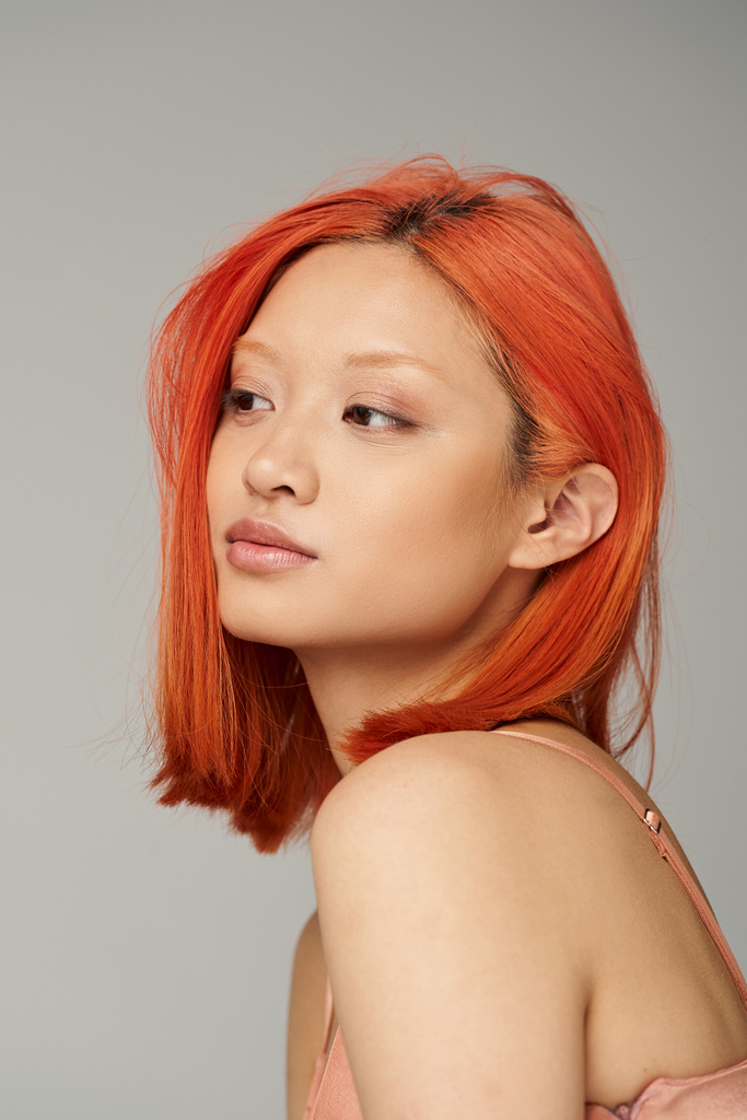 портрет витонченої молодої азіатки з ідеальною шкірою і рудим волоссям позує на сірому фоні - Фото, зображення