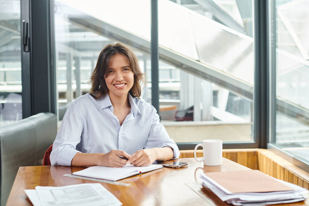 aantrekkelijke brunette vrouw in het bedrijfsleven casual kleding glimlachen en kijken naar camera, coworking - Foto, afbeelding