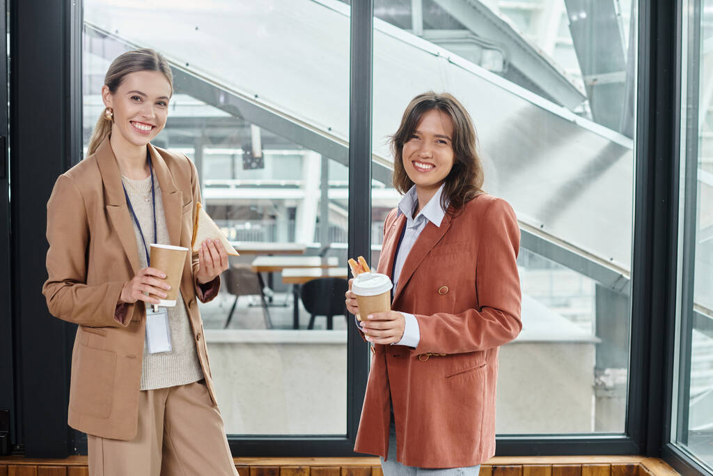 colegas elegantes em trajes casuais de negócios sorrindo e desfrutando de café e sanduíches, coworking - Foto, Imagem