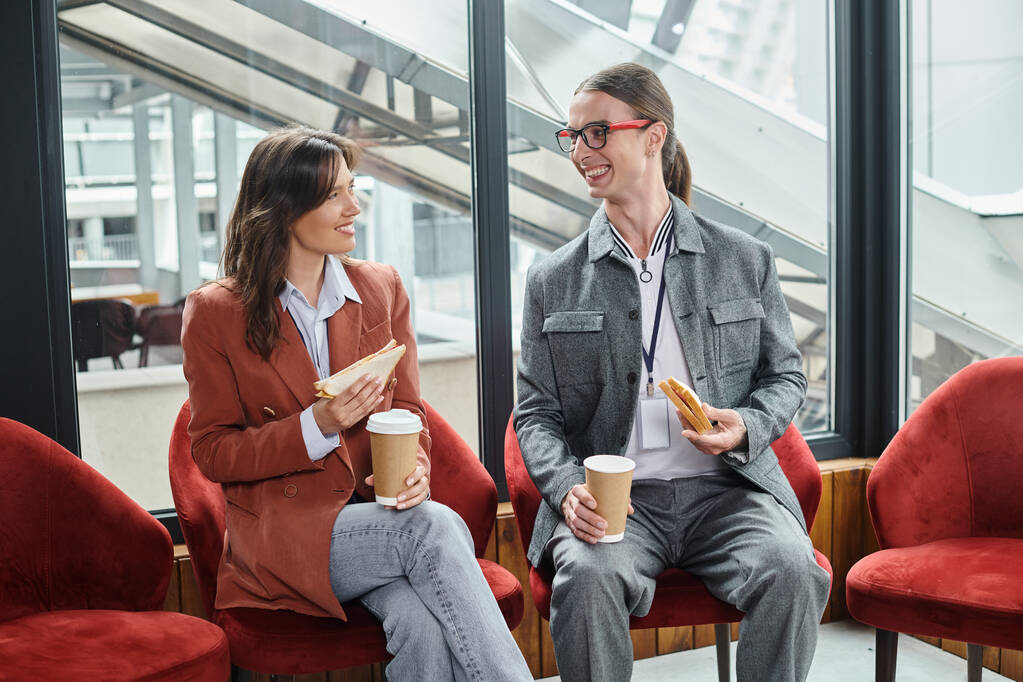 dois colegas de trabalho em trajes casuais inteligentes sentados em cadeiras conversando e comendo, conceito de coworking - Foto, Imagem