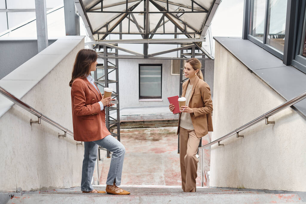 twee collega 's in zakelijke casual kleding staan op trappen glimlachend naar elkaar, coworking concept - Foto, afbeelding