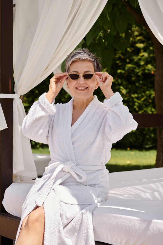 счастливая женщина средних лет в солнечных очках отдыхает в частном пляжном павильоне во время оздоровительного отдыха - Фото, изображение