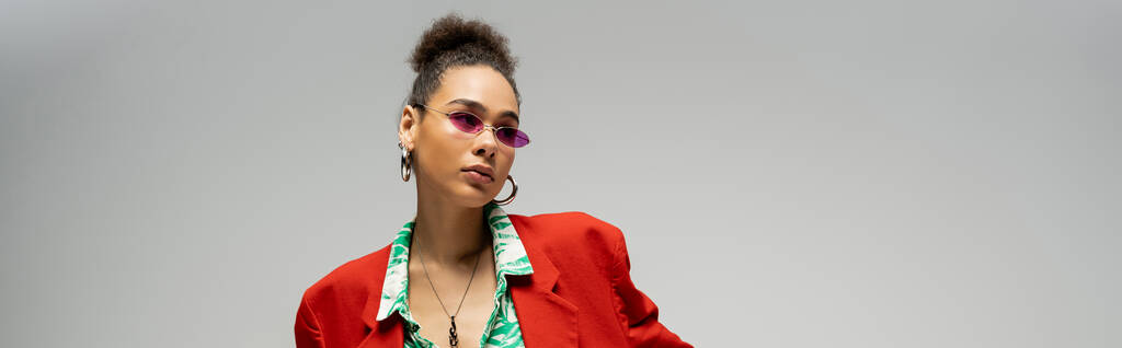 stylish african american woman in  pink sunglasses and trendy vibrant attire posing on grey, banner - Photo, Image