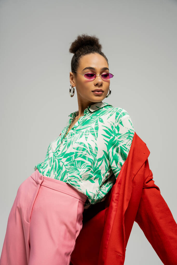 афроамериканська жінка в сонцезахисних окулярах і модний одяг позує на сірому фоні, особистий стиль - Фото, зображення