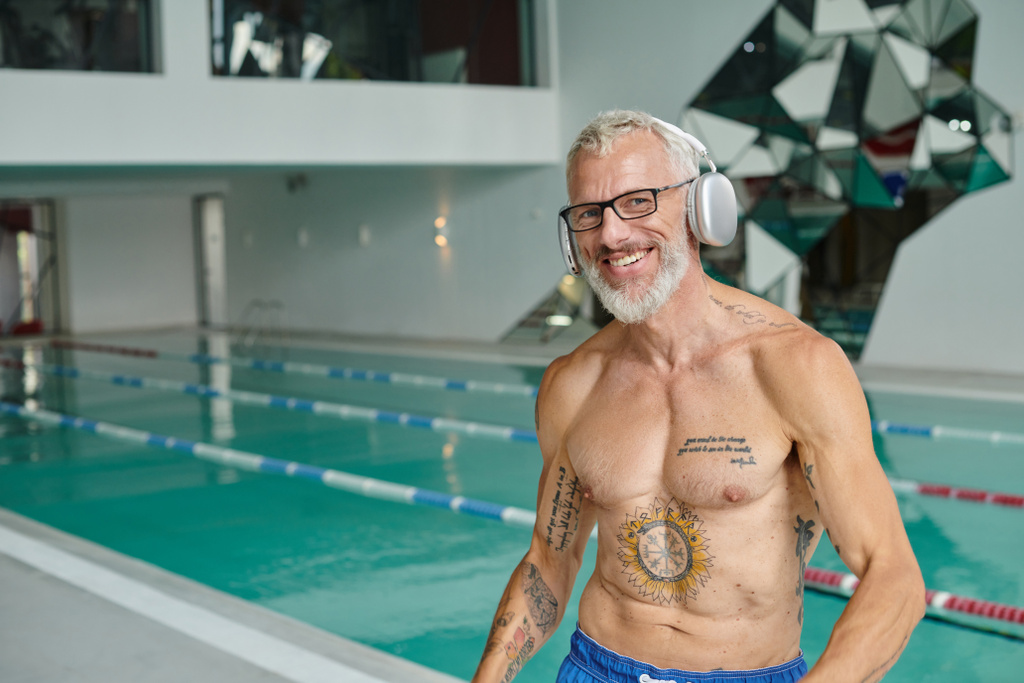 piacere e tatuato uomo di mezza età ascoltare musica in cuffie wireless nel centro benessere - Foto, immagini