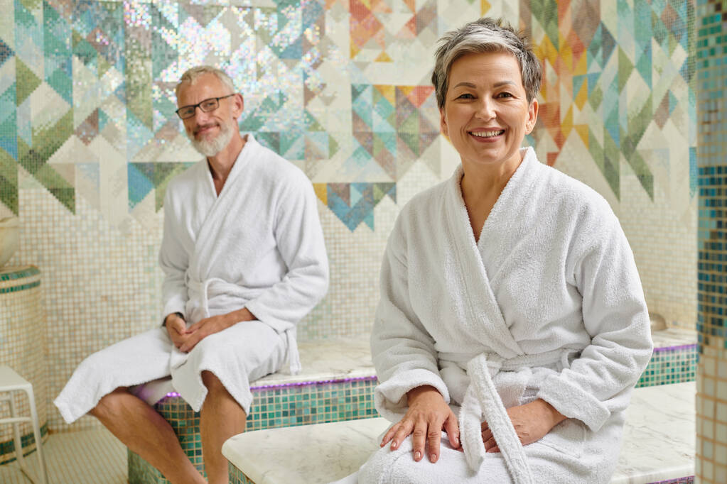feliz casal de meia-idade em vestes brancas sentado juntos na sauna de mármore, conceito de bem-estar spa - Foto, Imagem