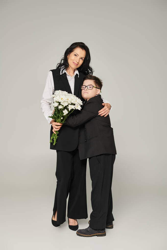 幸せな女性とダウン症候群を持つ男の子 花を保持し,灰色で抱擁, ユニークな家族 - 写真・画像