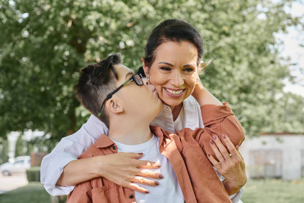 enfant avec le syndrome du duvet embrasser souriant mère d'âge moyen pendant la sortie du parc, moments heureux - Photo, image