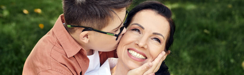 kid with down syndrome, in eyeglasses, kissing happy mother in park, emotional connection, banner - Photo, Image