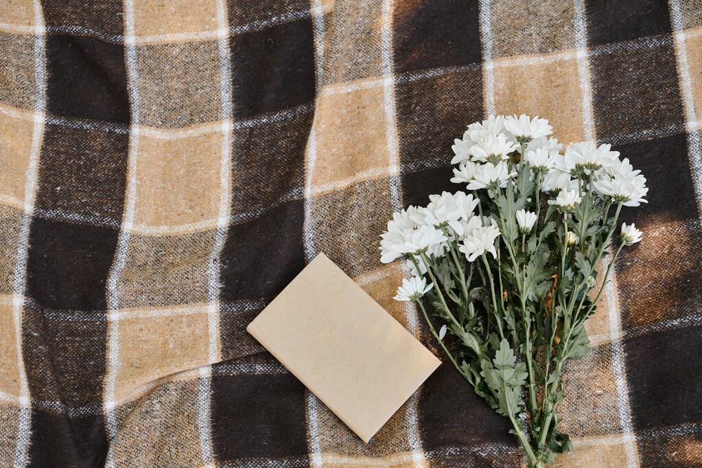 vista superior del libro y crisantemos blancos en manta de picnic a cuadros, concepto de tiempo de calidad - Foto, Imagen
