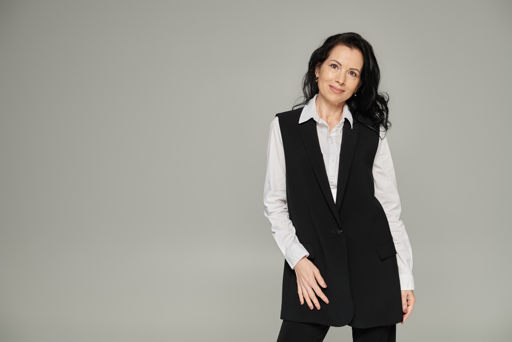 successful middle aged  businesswoman in stylish formal wear standing and smiling at camera on grey - Photo, Image