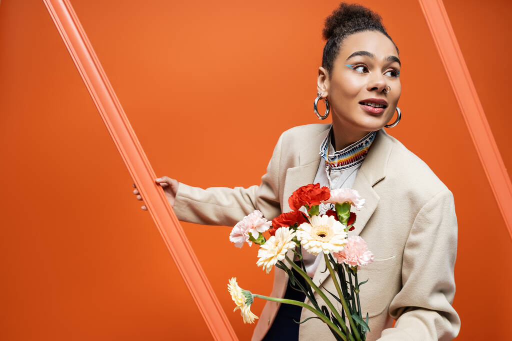 schicke stylische Fashionista im trendigen Straßenoutfit mit orangefarbenem Rahmen und Blumenstrauß - Foto, Bild