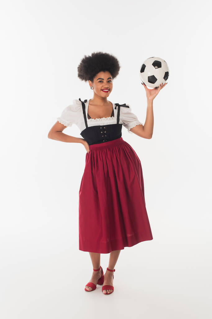 заманчивая африканская американская баварская официантка в аутентичном платье позирует с футбольным мячом на белом - Фото, изображение