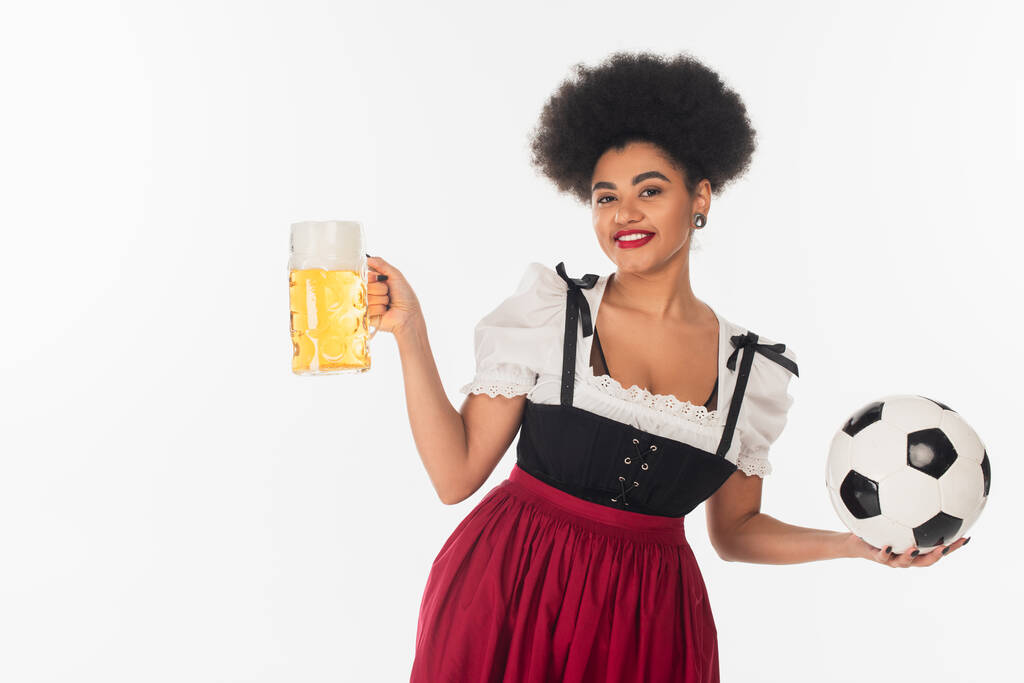 Afrykański amerykański oktoberfest kelnerka z piłką nożną i kubek piwa lager z pianką na białym - Zdjęcie, obraz
