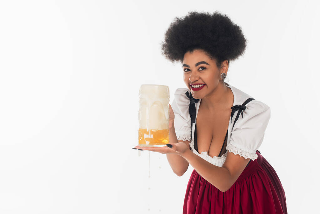 africano americano oktoberfest camarera celebración taza de cerveza con espuma y mirando la cámara en blanco - Foto, imagen