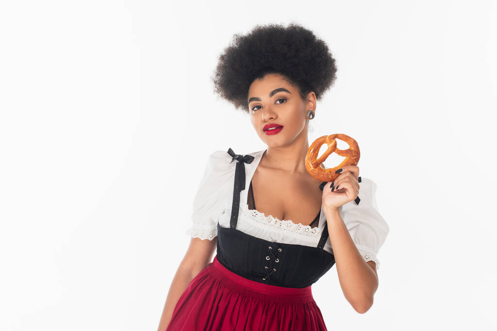 vrij Afrikaans amerikaans bavarian serveerster in oktoberfest outfit met heerlijke pretzel op wit - Foto, afbeelding