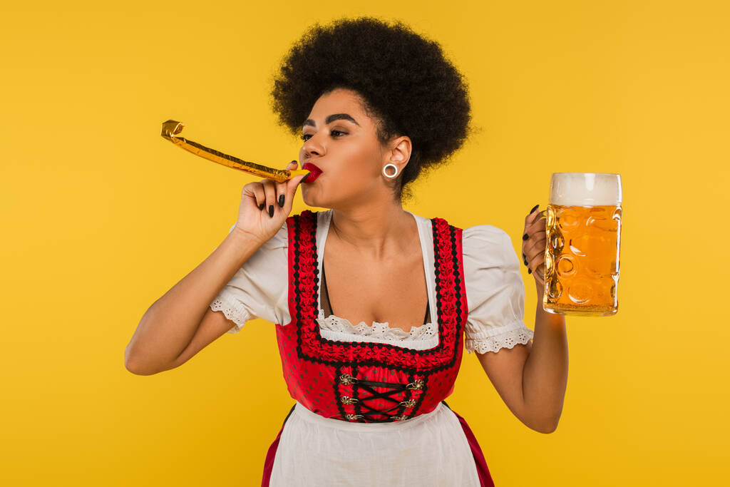 african american oktoberfest waitress with party horn and mug of craft foamy beer on yellow - Photo, Image