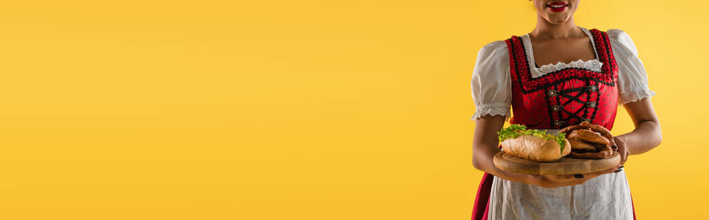 cultivada africana americana oktoberfest garçonete com deliciosos lanches na bandeja de madeira em amarelo, banner - Foto, Imagem