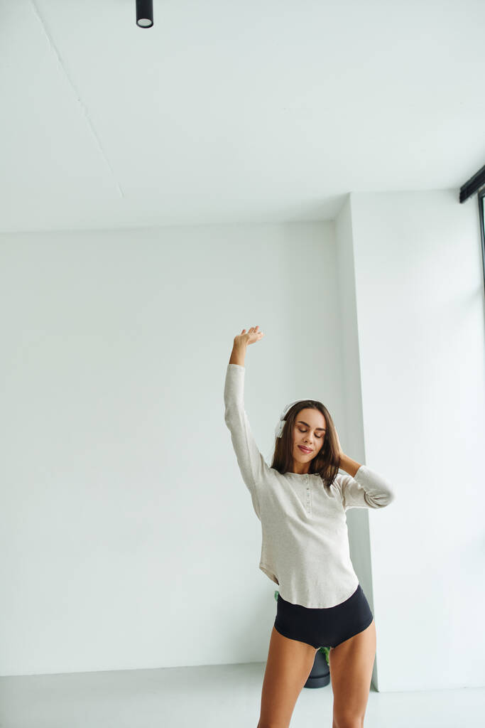 atraktivní brunetka žena v dlouhém rukávu a kalhotky tanec při poslechu hudby ve sluchátkách - Fotografie, Obrázek