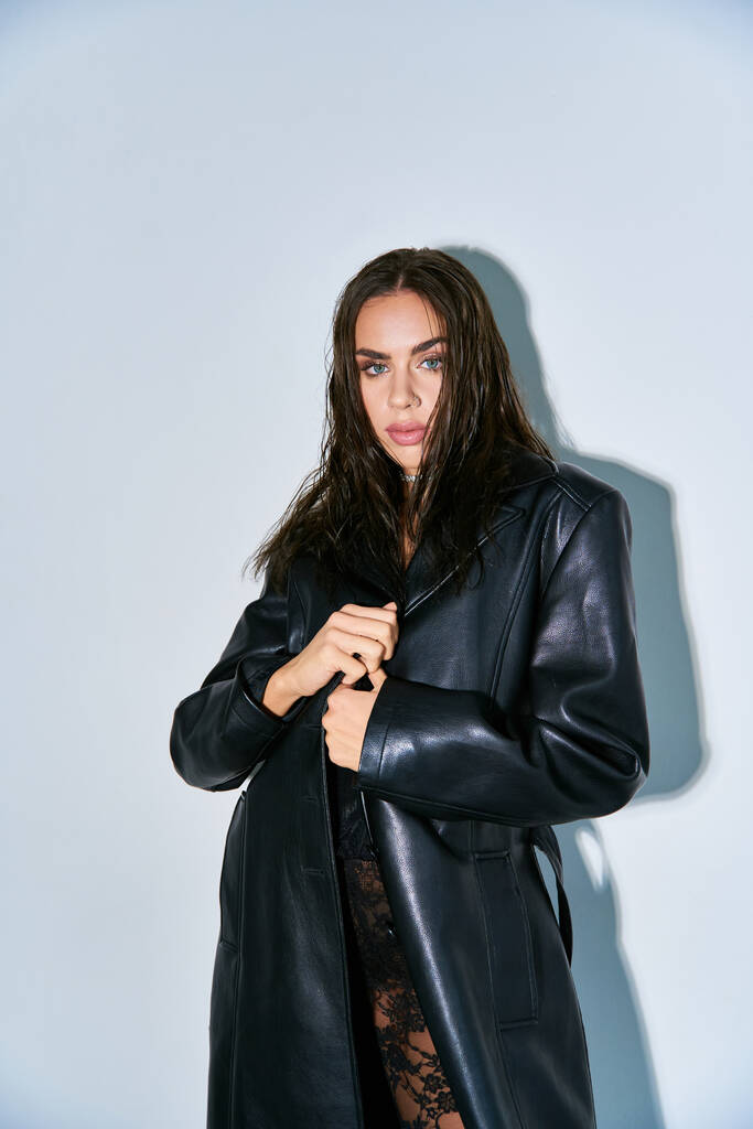 look sexy, mujer con el pelo moreno posando en ropa interior de encaje negro y abrigo de cuero sobre fondo gris - Foto, Imagen