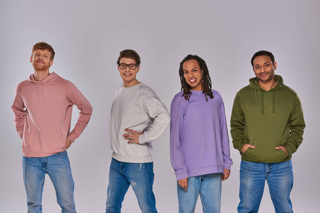 giovani amici multirazziali in abbigliamento casual in piedi con le mani akimbo su sfondo grigio, diversità - Foto, immagini