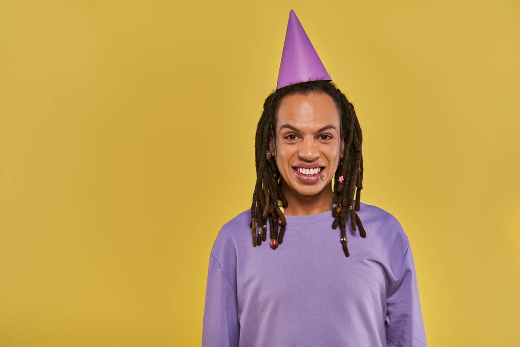 Веселый африканский американец в шляпе на день рождения и с проколотой губой, улыбающийся в камеру, день рождения - Фото, изображение