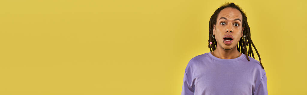 zaskoczony Afrykanin amerykański mężczyzna w fioletowej bluzie z przekłutą wargą na żółtym tle, sztandar - Zdjęcie, obraz