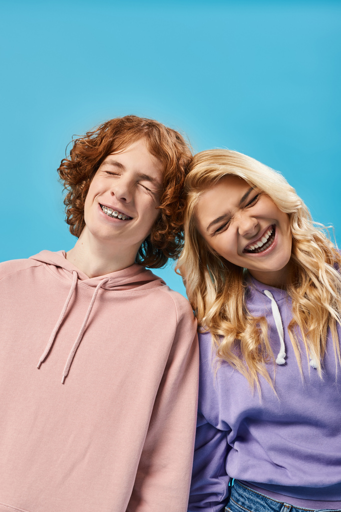 overjoyed teenage friends in stylish hoodies laughing with closed eyes on blue, carefree teens - Photo, Image