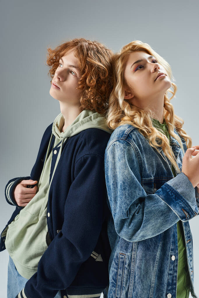 dreamy teen boy and girl in stylish casual wear standing back to back and looking away on grey - Photo, Image