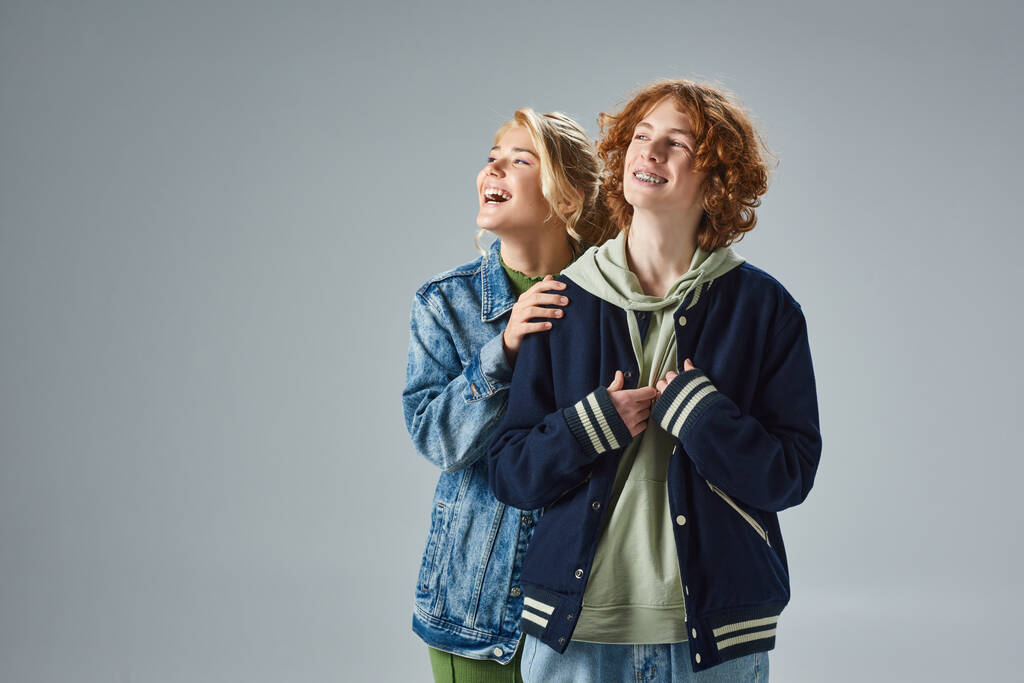 amigos adolescentes alegres en ropa casual de moda riendo mientras se mira hacia otro lado en gris, estilo de la calle - Foto, Imagen