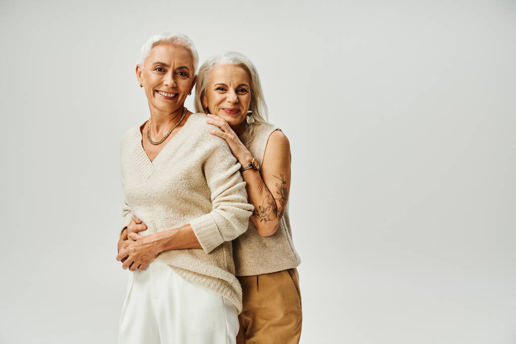 joyeuses femmes âgées en tenue décontractée à la mode regardant la caméra sur gris, beauté intemporelle - Photo, image