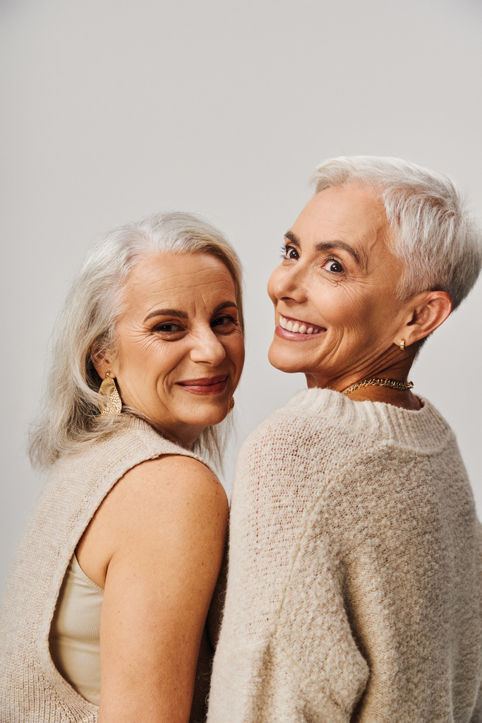χαρούμενες και στιλάτες ηλικιωμένες γυναίκες με ασημένια μαλλιά χαμογελαστά σε γκρι, ευτυχία και μοντέρνα γήρανση - Φωτογραφία, εικόνα