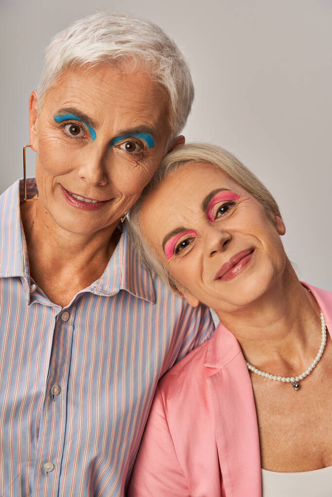 portrait de fashionistas seniors aux cheveux argentés et maquillage souriant à la caméra sur fond gris - Photo, image