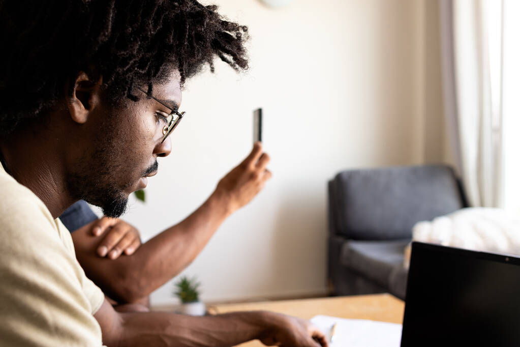 Черный парень в афро-волосах и очках использует ноутбук дома со своим напарником. - Фото, изображение