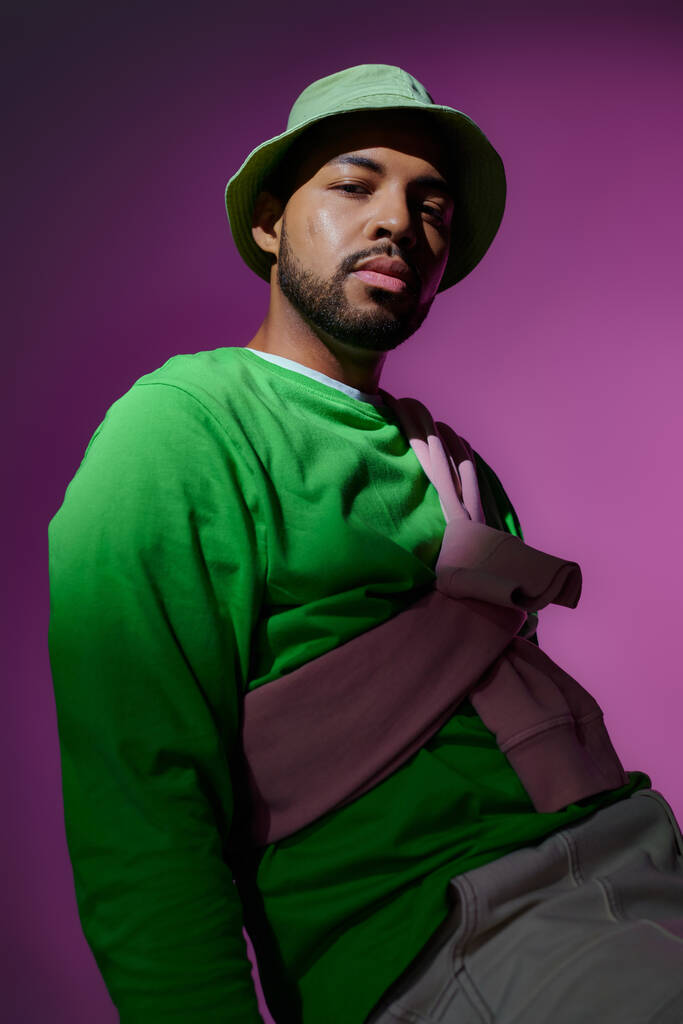 joven hombre guapo en panama verde con sudadera púrpura atada en sus hombros, concepto de moda - Foto, Imagen