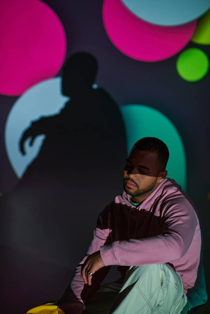 good looking man in pink hoodie sitting on floor in digital projector lights, fashion concept - Photo, Image