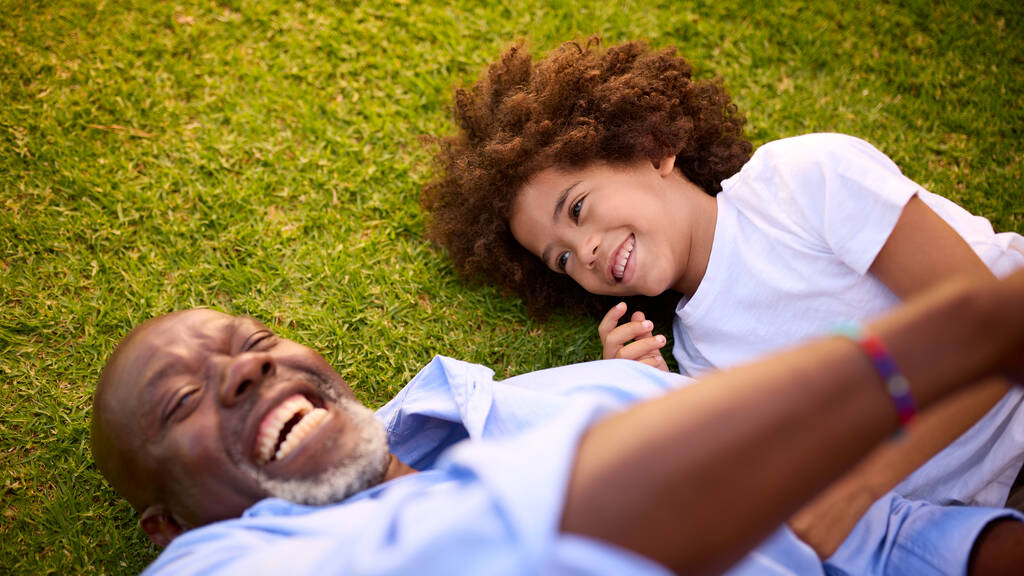 Выстрел любящего дедушки и внука, лежащих на траве и смеющихся вместе - Фото, изображение