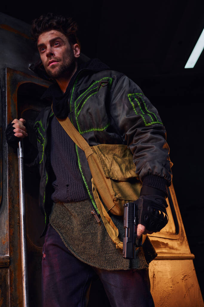 neoholený muž s poškrábanou tváří stojící s plátěnou taškou a pistolí v nebezpečném metru po katastrofě - Fotografie, Obrázek