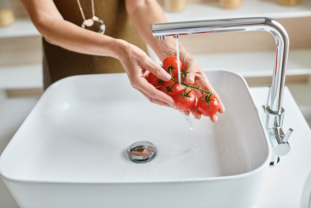 обрізаний знімок жінки, що миє свіжі та стиглі вишневі помідори вдома, жіночі руки тримають овочі - Фото, зображення