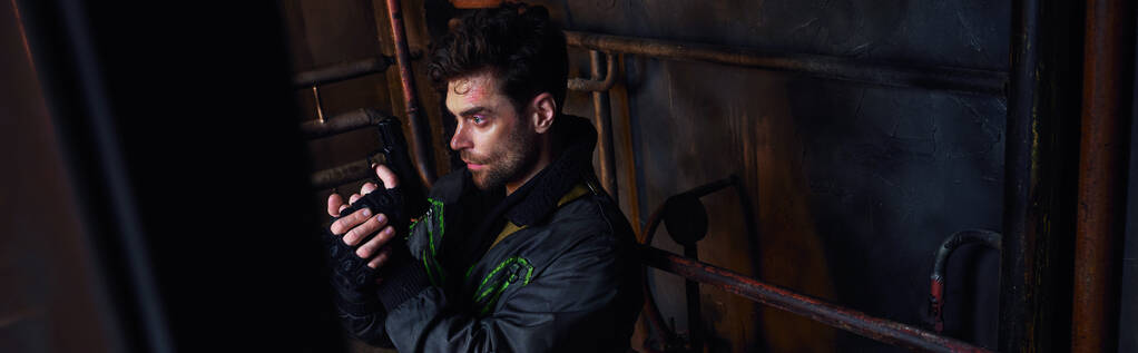 放棄された地下鉄,バナー,ゲームキャラクターの錆びたパイプライン近くの銃を目指す黒いジャケットの男 - 写真・画像