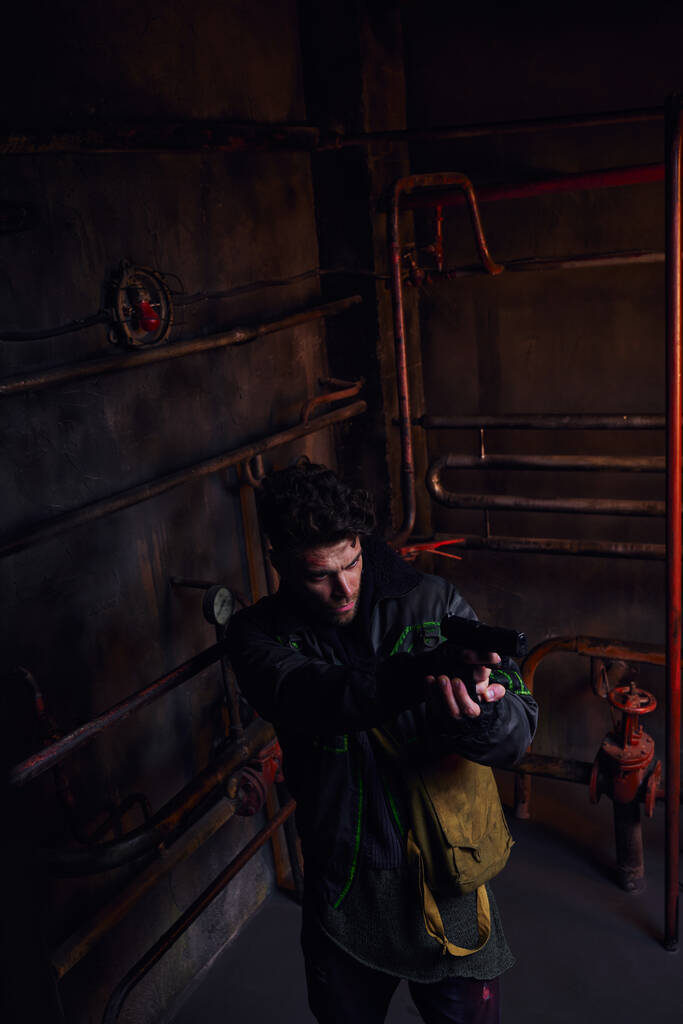 vysoký úhel pohledu na koncentrovaného muže mířícího pistolí v nebezpečném postapokalyptickém metru - Fotografie, Obrázek