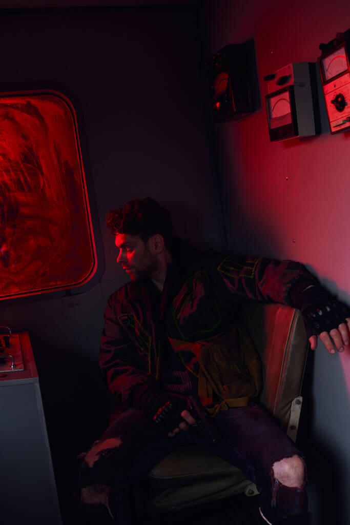 zrozpaczony mężczyzna z bronią w brudnym wagonie metra z czerwonym światłem, postacią po apokalipsie gry - Zdjęcie, obraz