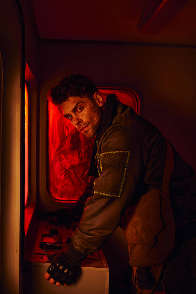 neoholený muž při pohledu na kameru poblíž palubní desky opuštěného kočáru v post-apokalyptickém metru - Fotografie, Obrázek