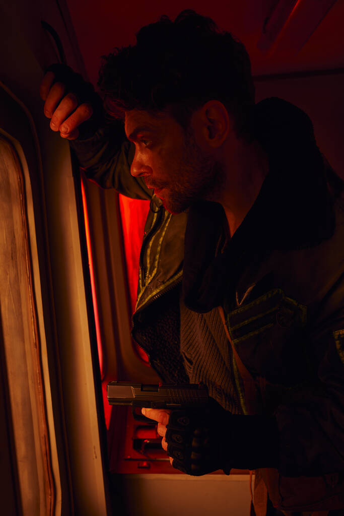 Человек с пистолетом смотрит в грязное окно заброшенного вагона метро, постапокалиптическое выживание - Фото, изображение