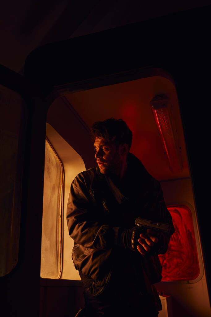 keskittynyt mies aseen kanssa katselee kameraa metrovaunuissa katastrofin jälkeisessä metrossa punaisessa valossa - Valokuva, kuva