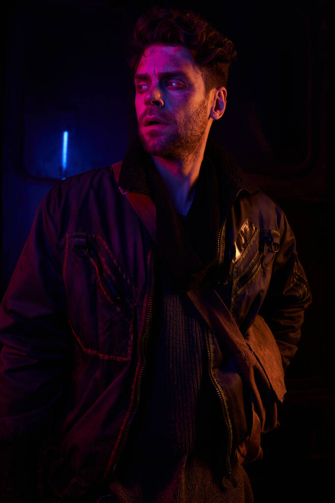 uomo teso in giacca nera distogliendo lo sguardo nel buio del tunnel sotterraneo abbandonato con luce al neon - Foto, immagini