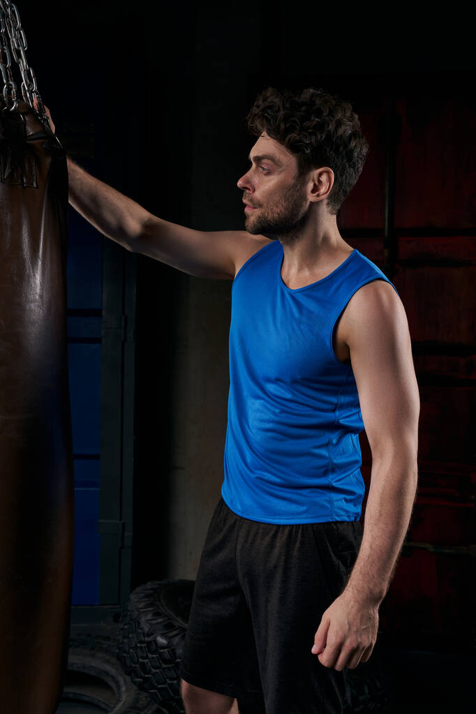 sportieve man in blauwe tank top staan in de buurt boksbal op straat 's nachts - Foto, afbeelding