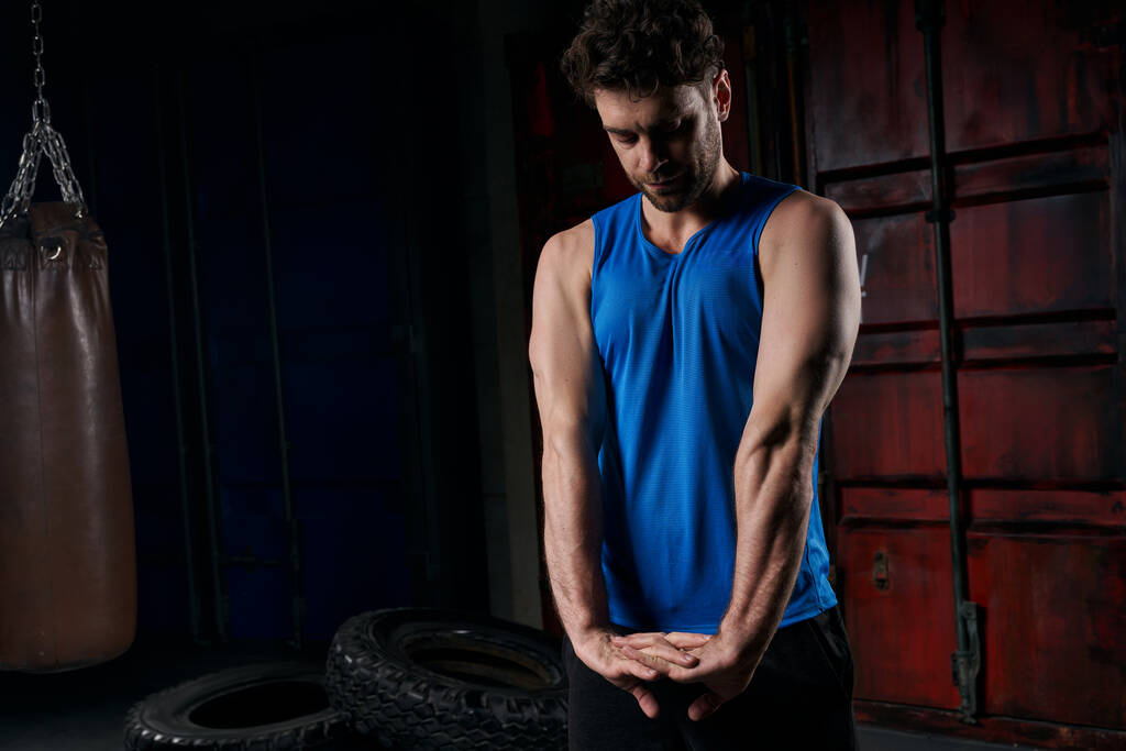athletischer Mann in blauem Tanktop, der nachts auf der Stadtstraße trainiert und die Arme ausstreckt - Foto, Bild